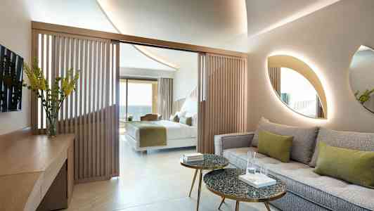 Et hotellrom med en sittegruppe, bord og en seng i bakgrunnen. (AI-generert tekst)