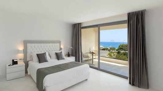 Et soverom med en dobbeltseng og utsikt over havet gjennom store vinduer. (AI-generert tekst)