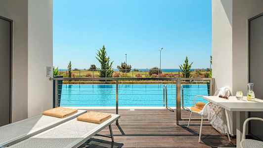 Utsikt fra terrasse over et basseng, med strand og hav i bakgrunnen. (AI-generert tekst)