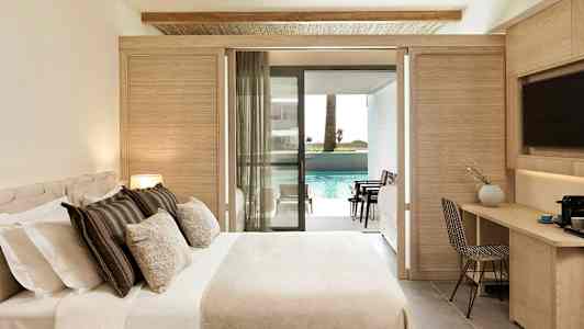 Et hotellrom med seng, skrivebord og en balkong som fører til et basseng. (AI-generert tekst)