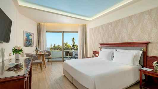 Et hotellrom med en dobbeltseng, sittegruppe og stor balkong med utsikt. (AI-generert tekst)