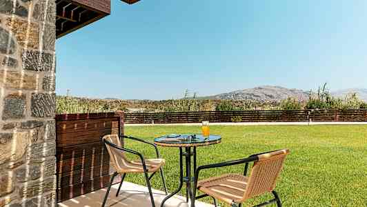 Utendørsområde med bord og to stoler, gressplen og fjell i bakgrunnen. (AI-generert tekst)