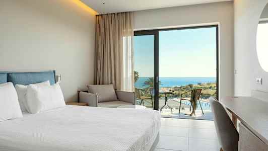 Hotellrom med seng, sofa og utsikt over havet. (AI-generert tekst)