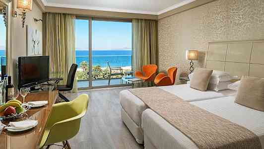 Hotellrom med senger, sittemøbler og utsikt over havet. (AI-generert tekst)