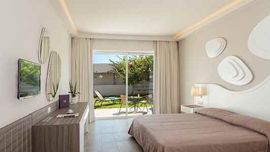 Et hotellrom med en dobbeltseng, skrivebord og utsikt mot et privat hageområde med møbler gjennom glassdører. (AI-generert tekst)