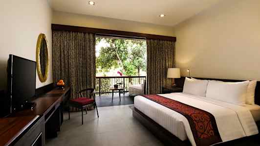 Et hotellrom med en stor seng, et skrivebord med et gullspeil og en TV. Vinduet åpner ut mot en balkong med utsikt over grønne trær. (AI-generert tekst)