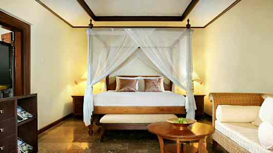 Et soverom med en seng med sengehimmel, to nattbord og en liten sofa foran et bord. (AI-generert tekst)