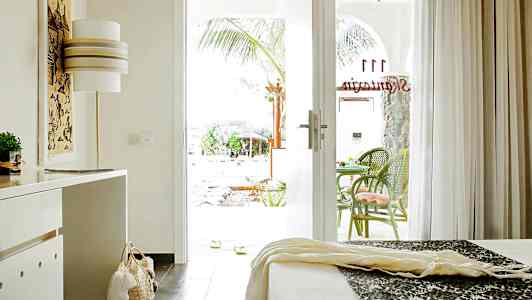 Et hotellrom med en åpen glassdør til en terrasse med grønne stoler. (AI-generert tekst)