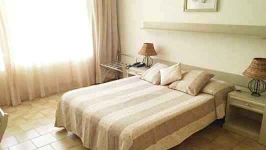 Et hotellrom med en dobbeltseng, to nattbord og en lampe. (AI-generert tekst)