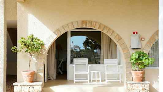 En terrasse med to hvite stoler og bord foran en vindusbue. (AI-generert tekst)