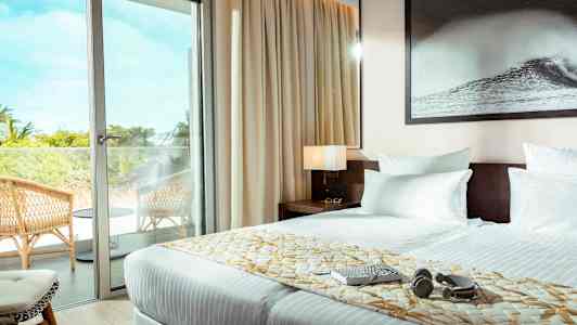 Et hotellrom med en dobbeltseng, en glassdør som fører ut til en balkong med stoler. (AI-generert tekst)