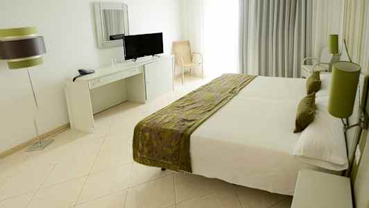 Rom med en dobbeltseng, skrivebord med speil og TV, samt en bordlampe. (AI-generert tekst)