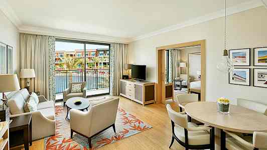 Et hotellrom med en stue, spisebord og en balkong som vender mot et utendørs basseng. (AI-generert tekst)