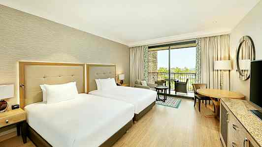 Hotellrom med to senger og møbler, samt en balkong med utsikt. (AI-generert tekst)