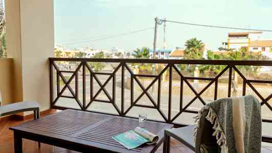 En balkong med bord og stoler, med utsikt over en gate og bygninger. (AI-generert tekst)