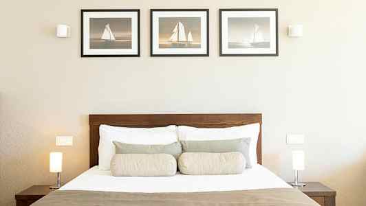 Et soverom med en seng, to lamper på nattbord og tre bilder på veggen. (AI-generert tekst)