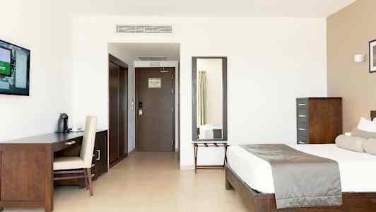 Et moderne hotellrom med seng, skrivebord, TV og speil. (AI-generert tekst)