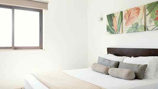 Bilde av et lyst soverom med en dobbeltseng, dekorative puter og veggdekorasjon over sengen. (AI-generert tekst)