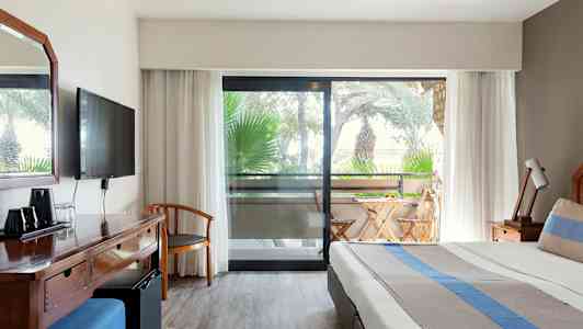 Bilde av hotellrom med seng, skrivebord og balkong med utemøbler. (AI-generert tekst)