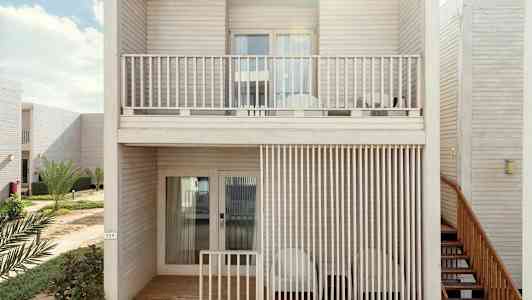 To etasjer med leilighetsbalkonger i tredesign, omgitt av grøntområder. (AI-generert tekst)