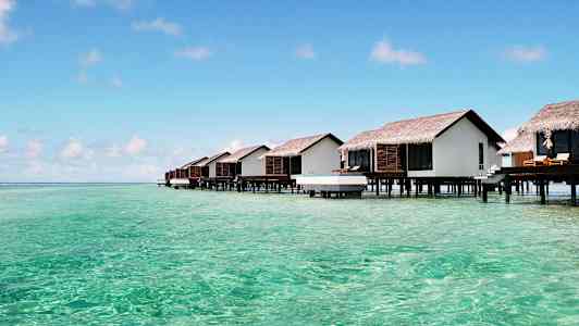 Hytter på stolper over turkis vann. (AI-generert tekst)