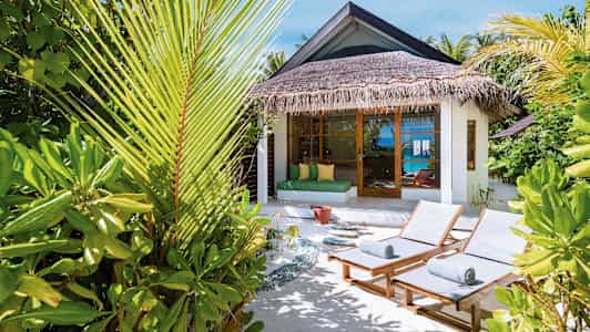 Solstoler og tropiske planter ved en bungalow med havutsikt. (AI-generert tekst)