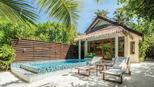 En bungalow med stråtak, et lite basseng og solsenger, omgitt av frodig planter. (AI-generert tekst)