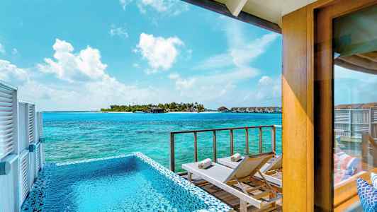 Utsikt fra en terrasse med basseng og solsenger mot havet og en øy med bungalower. (AI-generert tekst)