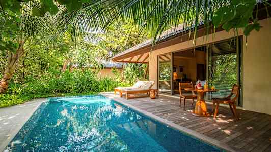 Et privat basseng ved en tropisk villa med en solseng og et bord med stoler. (AI-generert tekst)