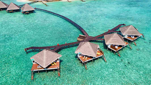 Bungalower på pæler over turkis vann, forbundet med trebroer. (AI-generert tekst)