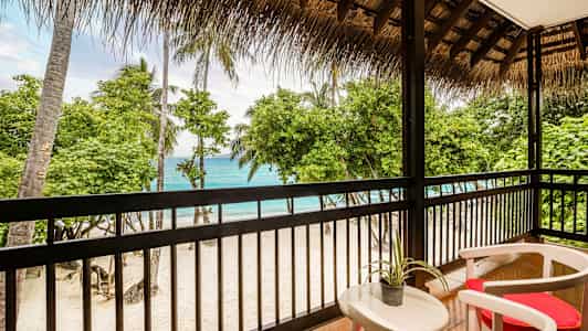 Utsikt fra en terrasse mot en sandstrand med palmer og hav. (AI-generert tekst)