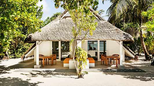 En bungalow med stråtak, omgitt av trær og vegetasjon, med havutsikt i bakgrunnen. (AI-generert tekst)