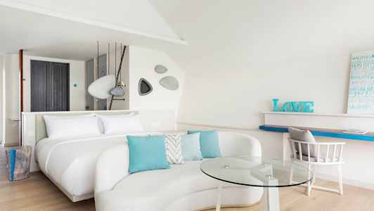 Et moderne og lyst hotellrom med en stor seng, sofagruppe med glassbord og arbeidsområde. (AI-generert tekst)