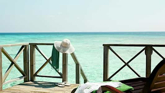 Treterrasse ved sjøen med en hvit solhatt og et grønt klesplagg hengende på rekkverket. (AI-generert tekst)