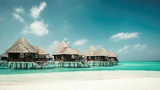 Bungalower på påler over blått vann ved en strand. (AI-generert tekst)