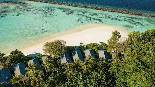 En vakker utsikt med strand, hav, korallrev og bungalower omgitt av trær. (AI-generert tekst)