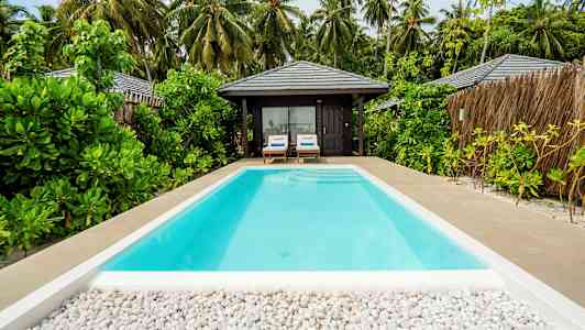 Et svømmebasseng med utsikt til en tropisk bungalow og omkringliggende vegetasjon. (AI-generert tekst)