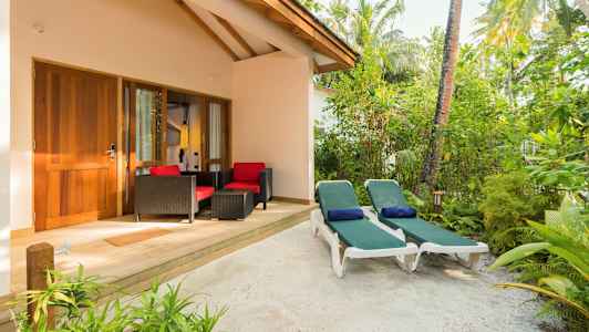 En uteplass med to solsenger og sittegruppe foran en bygning omgitt av vegetasjon. (AI-generert tekst)