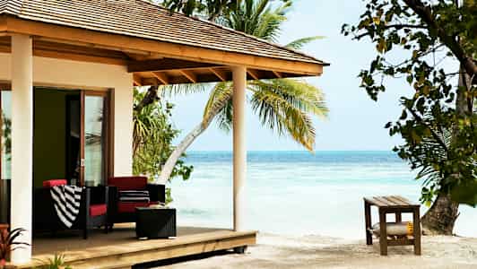 Strandvilla med veranda møblert med sofaer, bord og dekorert med palmer rundt. (AI-generert tekst)