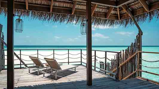 To solsenger på en trebro med utsikt over en klarblå kyst under et stråtak. (AI-generert tekst)