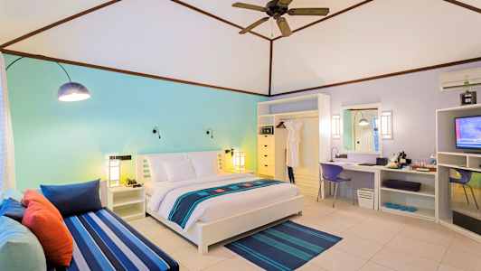 Et lyst hotellrom med en dobbeltseng, fargerik dekor og en sittegruppe. (AI-generert tekst)