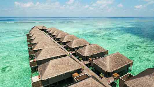 Bildet viser en rekke vannbungalower med stråtak, bygget på stylter over en turkis lagune. (AI-generert tekst)