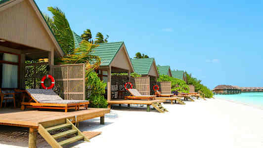 Strandbungalower med grønne tak og solsenger ved vannet. (AI-generert tekst)