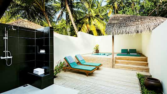 Utendørs dusj ved siden av solsenger og boblebad på en terrasse av tre omgitt av palmer. (AI-generert tekst)