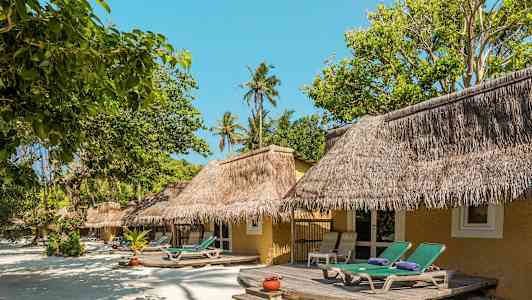 Strandbungalow med stråtak og solsenger foran omgitt av grøntområder. (AI-generert tekst)