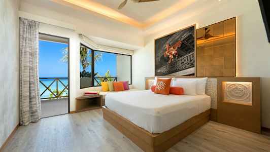 Et moderne hotellrom med en stor seng, fargerike puter, romslige vinduer og utsikt over havet. (AI-generert tekst)