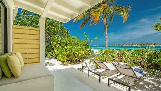 En terrasse ved stranden med solsenger, en palme og utsikt over havet. (AI-generert tekst)