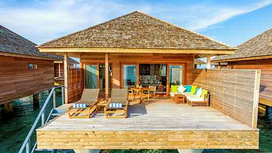 En overwater-bungalow med treterrasse og sittemøbler. (AI-generert tekst)