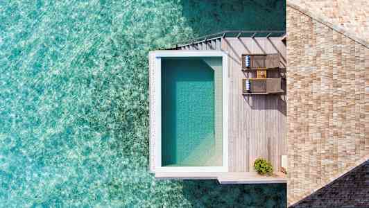 Et bilde ovenfra av et bassengområde med tredekke ved vannet. (AI-generert tekst)