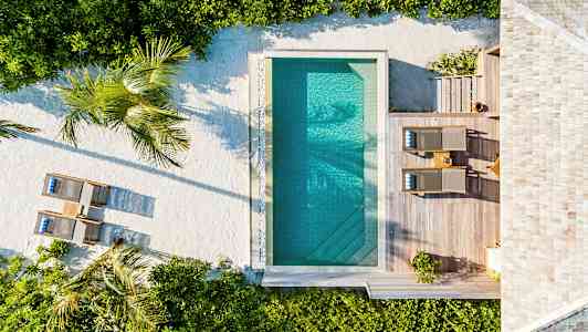 Luftfoto av et basseng med omkringliggende terrasse, solsenger og planter. (AI-generert tekst)